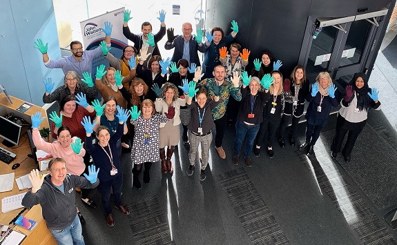 Members of the John Walton Muscular Dystrophy Research Centre wave their hands in the air wearing different coloured medical gloves.
